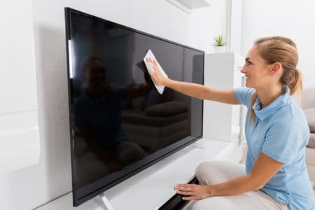 Smiling woman wiping television with a cloth in the living room