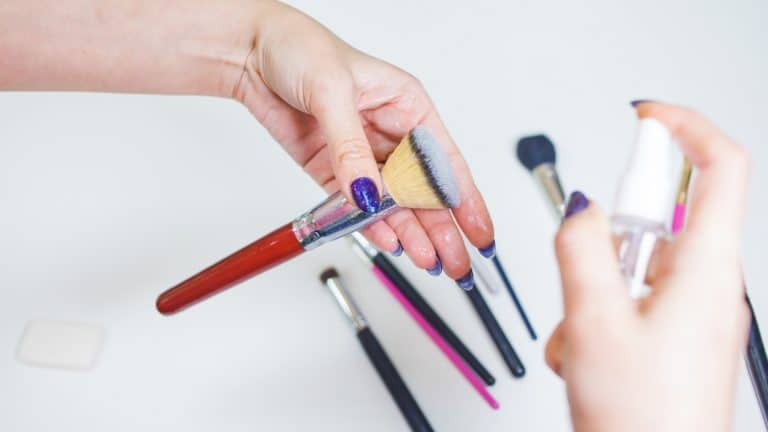 Woman's hands cleaning makeup brush using spray