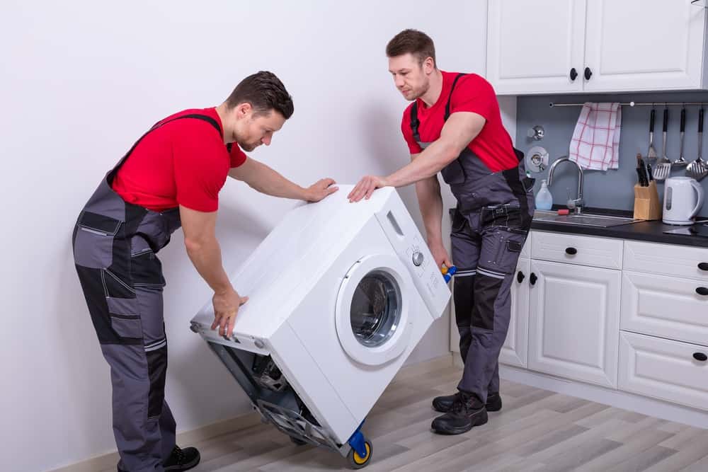 Two repairmen in red moving a front load washer