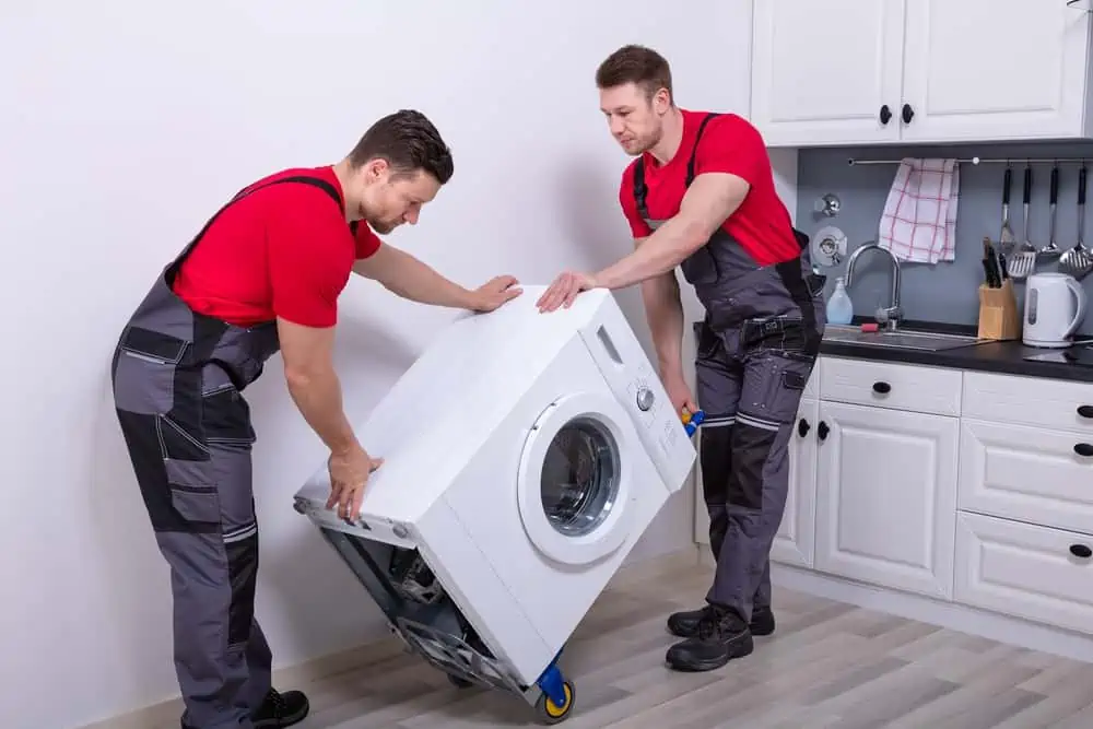 Two repairmen in red moving a front load washer
