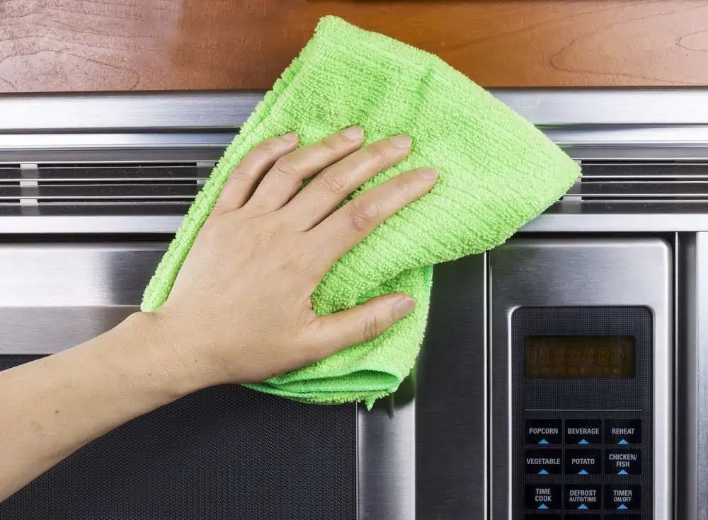 Hand with microfiber towel cleaning vents of microwave oven
