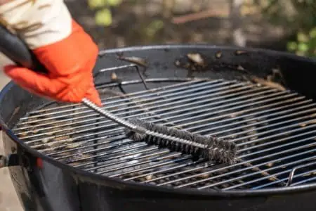 Male hand wearing red gloves cleaning dirty round grill with stiff brush