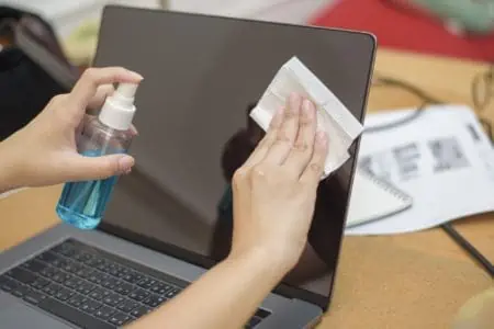 Woman wiping macbook screen with wipes and alcohol spray