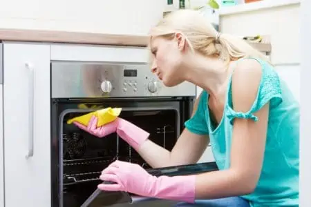 Young lady in gloves cleaning oven in the kitchen