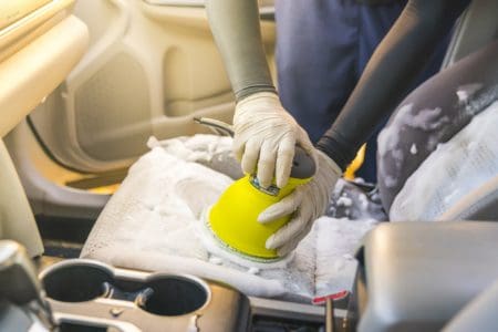 Man cleaning car seat by using foam chemical and scrubbing machine