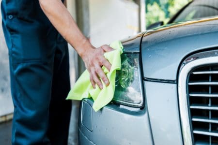 Cropped photo of man wiping car headlight with neon towel