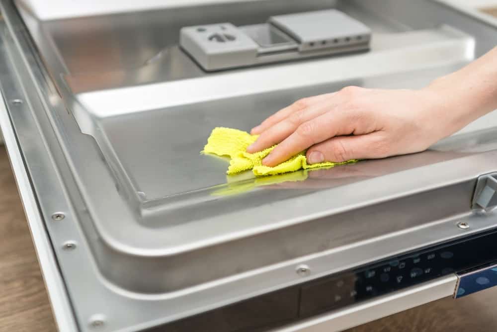 Woman's hand wiping stainless steel with yellow microfiber cloth