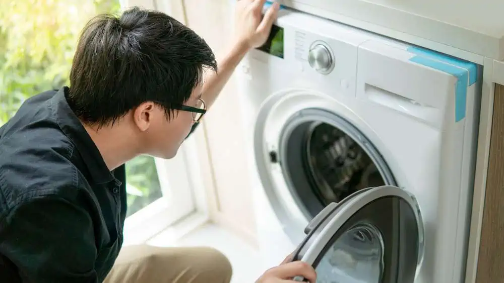 Guy with eyeglasses looking into front load washing machine
