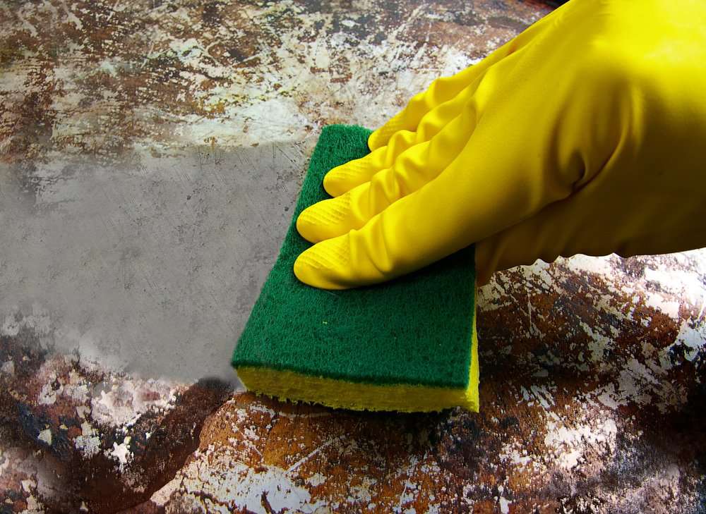 Hand in yellow gloves cleaning burnt pan using sponge