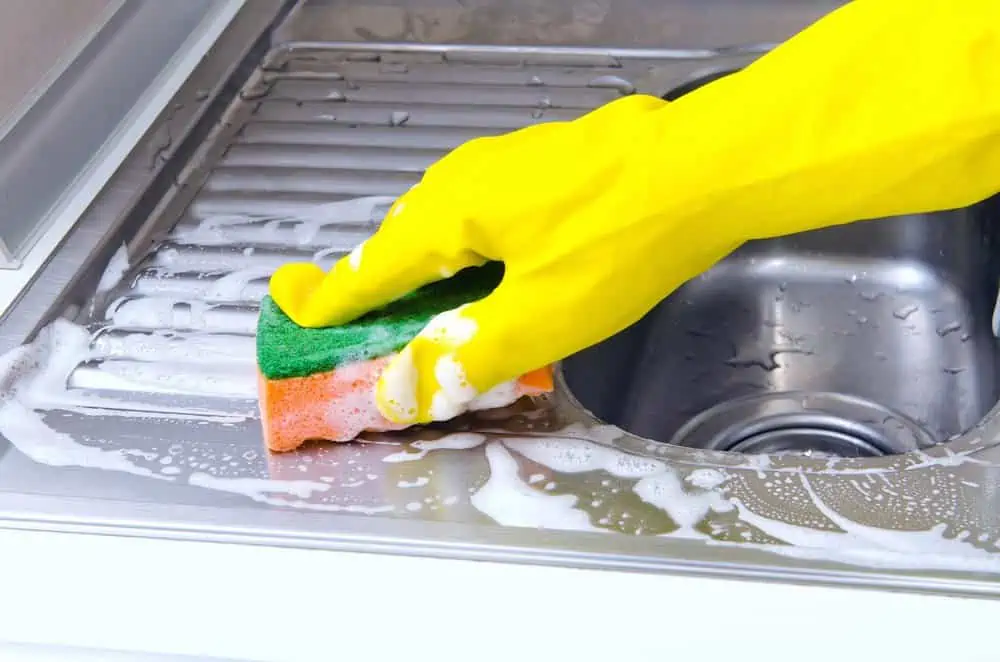 Hand in yellow gloves scrubbing the stainless steel sink with sponge