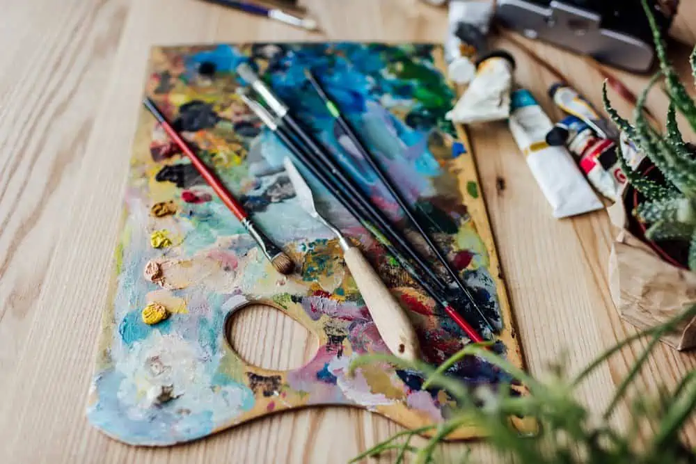 Palette with multiple paint and paint brushes on wooden table