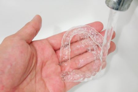Hand holding clear mouth guard under flowing water in the sink