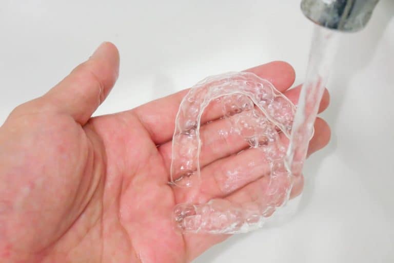 Hand holding clear mouth guard under flowing water in the sink