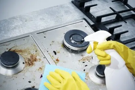 Hand in yellow gloves holding spray and microfiber cloth cleaning gas stove top