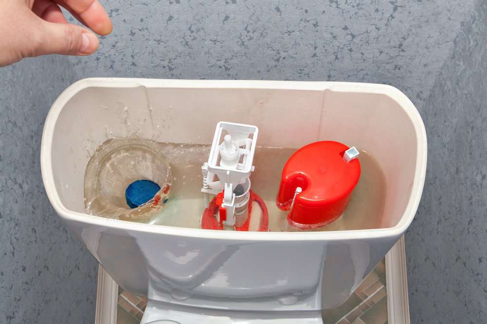 Hand throws a blue cleaner tablet in the toilet tank with water