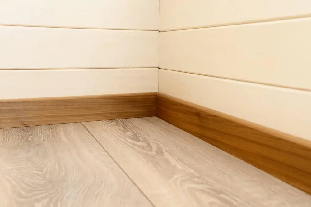 Corner of the room with wood baseboards, wooden wall and floor
