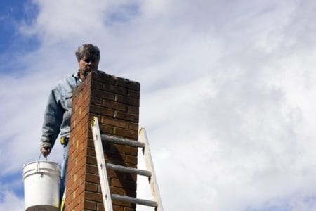 Man on ladder holding bucket repairing chimney on cloudy day