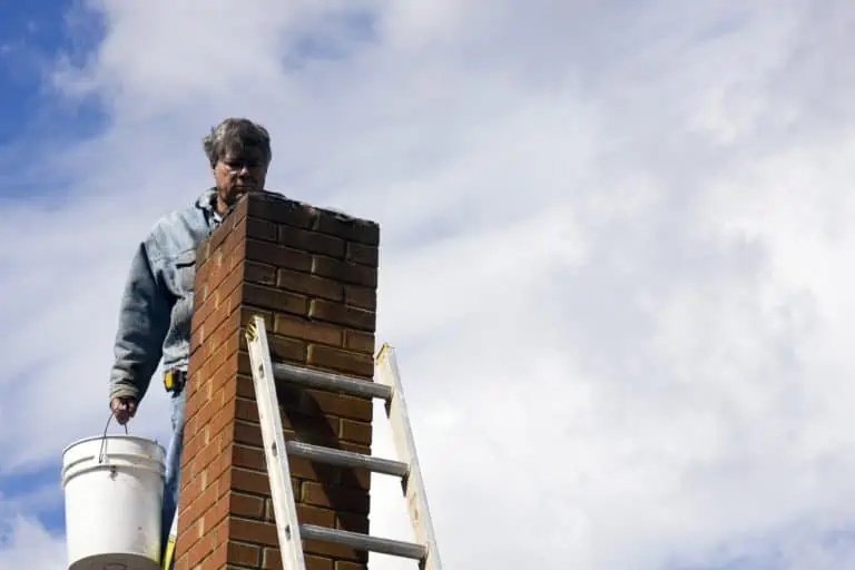 Man on ladder holding bucket repairing chimney on cloudy day
