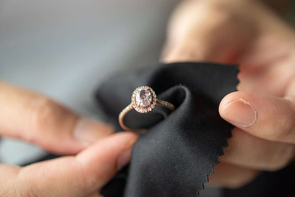 Man's hand cleaning gold ring with diamonds using black fabric cloth