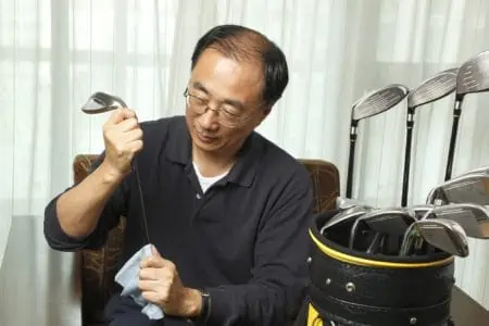 Asian man cleaning golf club with cloth at home