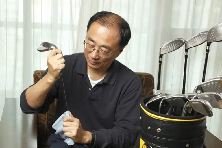 Asian man cleaning golf club with cloth at home
