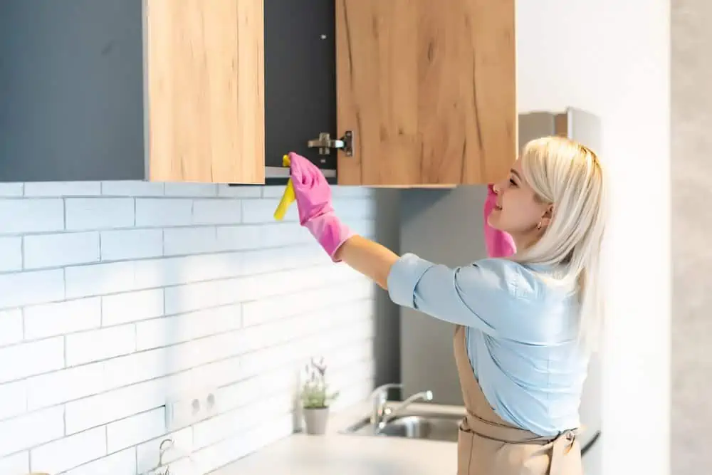 Woman in pink gloves opening the door of wooden kitchen cabinet