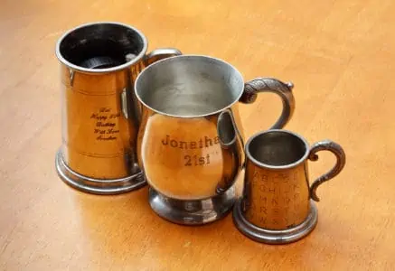 Three pewter mugs with engraved letters placed on top of wooden table