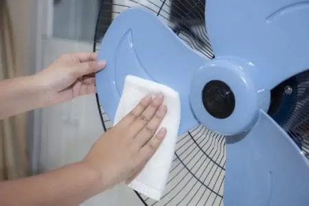 Female hand cleaning dirty electric fan blade with white cloth