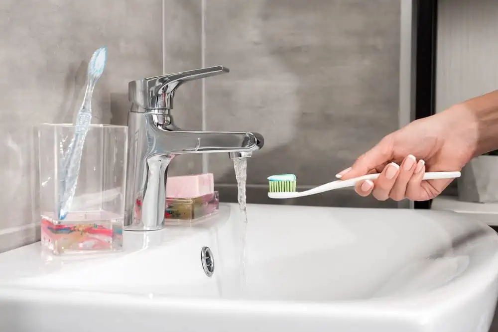 Female hand holding toothbrush in the sink with running water