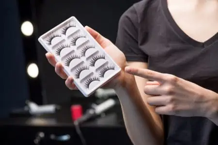Lady holding and pointing box with five pairs of false eyelashes