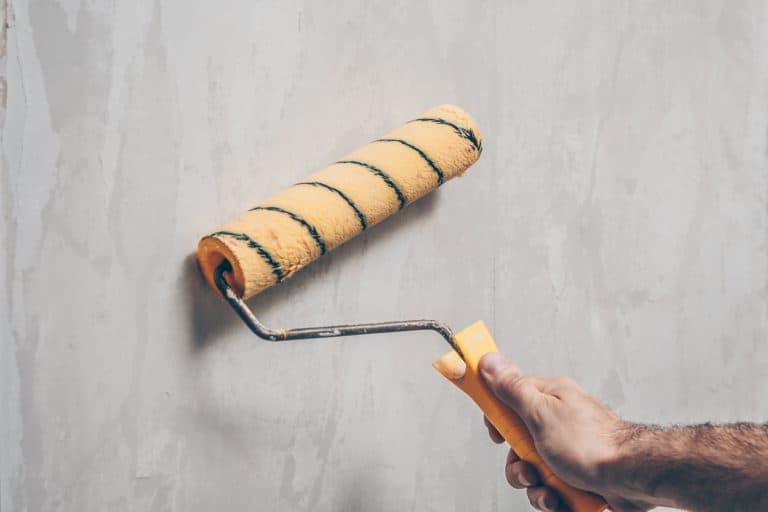 Male hand holding yellow paint roller priming the wall