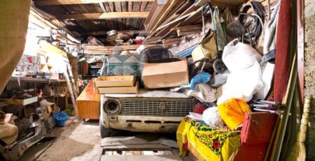 Old broken car and shelves with tools and stacks of things in the garage