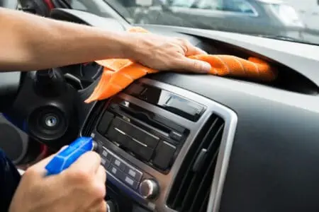 Male hand cleaning car dashboard using orange cloth