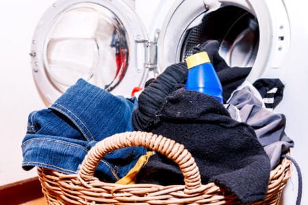 Dirty cloth in wooden basket with detergent in front of washing machine