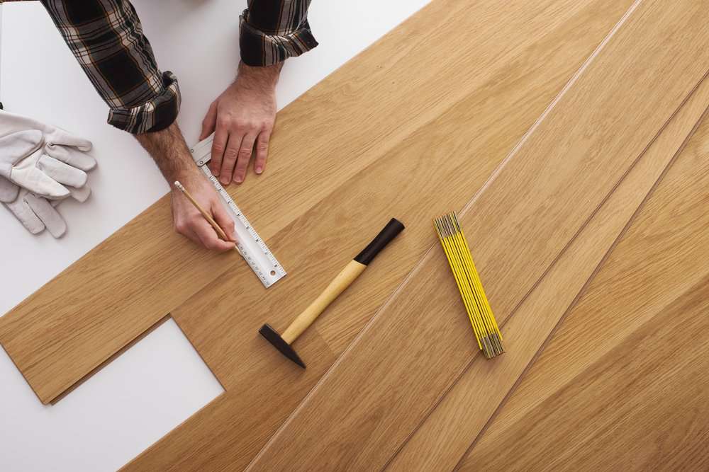 Man installing wooden flooring and measuring with a precision ruler