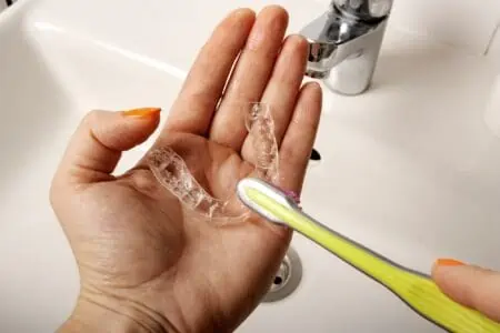 Female hand cleaning clear dental retainer using toothbrush in the sink