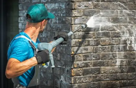 Man cleaning house brick wall using pressure washer