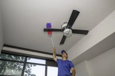 Man on ladder cleaning the blades of a ceiling fan