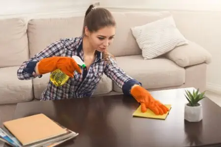 Woman cleaning wooden living room table using spray cleaner