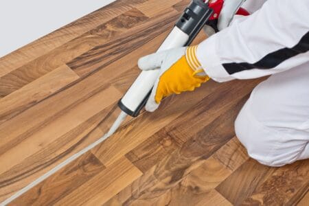 Man applying silicone sealant spaces of old wooden floor