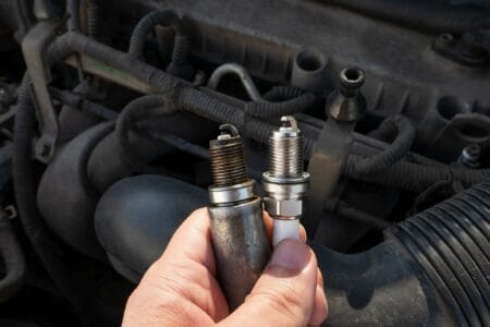 Man holding dirty and clean spark plugs