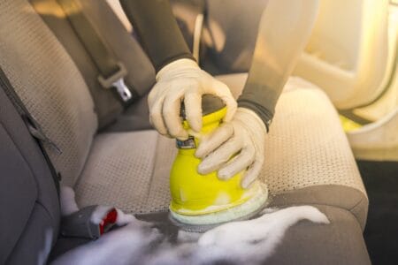 Man cleaning car interior by use foam chemical and scrubbing machine