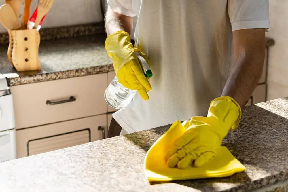 Man cleaning granite countertop with yellow cloth and spray cleaner