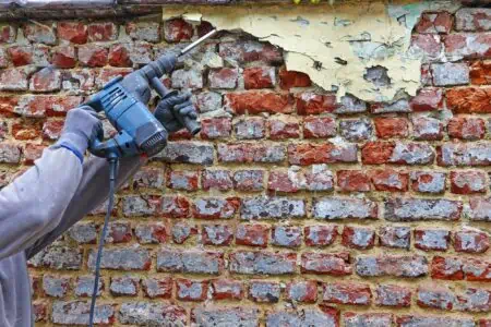 Male worker cleaning red brick wall outdoor using electrical hammer