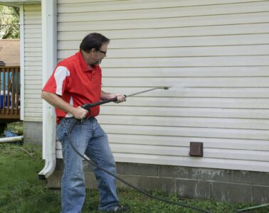 Male contractor removing algae from the house exterior with vinyl siding using pressure washer