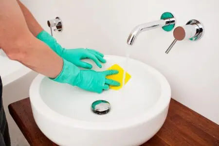 Man cleaning bathroom sink with yellow rag
