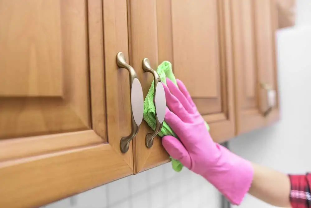 Female wearing gloves cleaning wood cabinet with green cloth