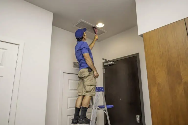 Handyman on ladder cleaning home air duct