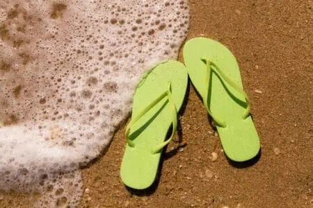 Bright green flip flops on the sand with ocean water