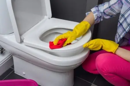 Woman wearing gloves cleaning the toilet seat with cloth